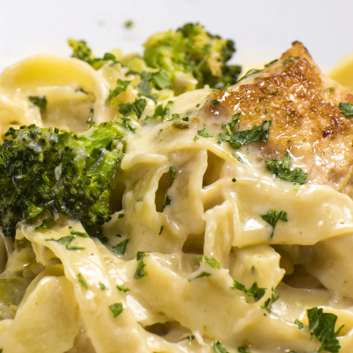 Golden, creamy Chicken Alfredo with broccoli and fettuccine, garnished with fresh parsley on a rustic wooden table.