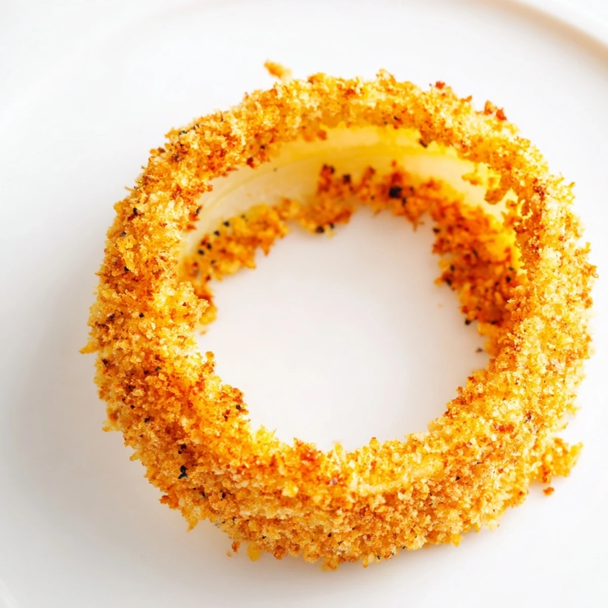 A hand dipping a crispy baked onion ring into a small bowl of spicy ranch dip.