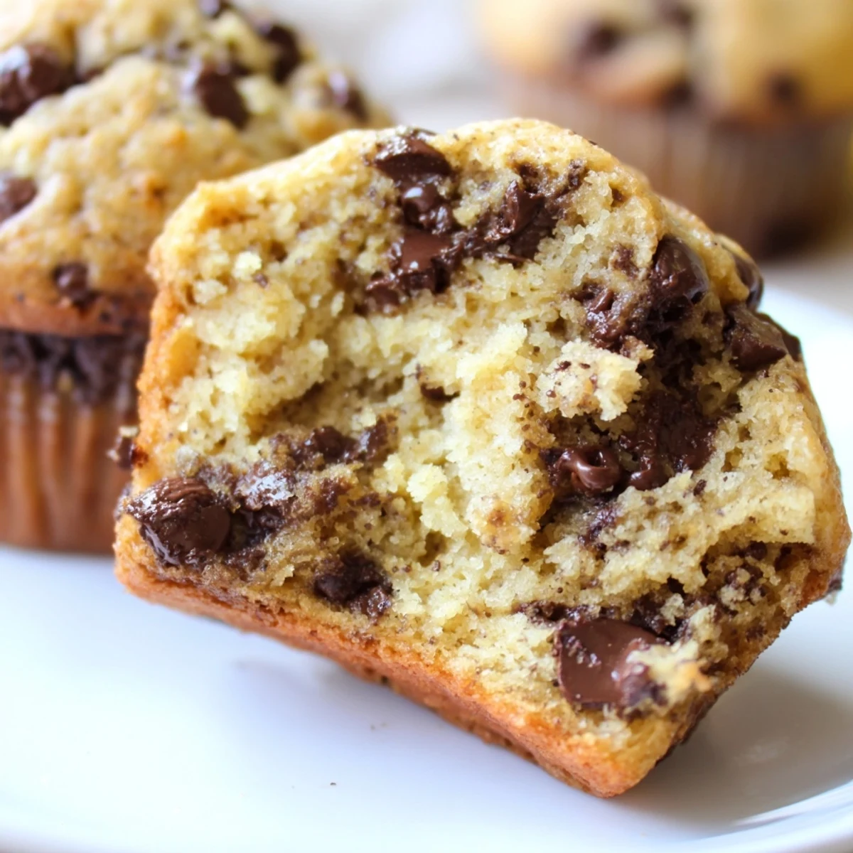 A close-up of Chocolate Chip Banana Bread Muffins with golden tops and gooey chocolate pooling on the surface.