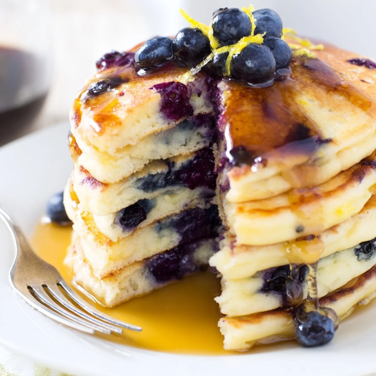 Golden lemon blueberry pancakes on a plate, topped with extra berries and a drizzle of sweet syrup.