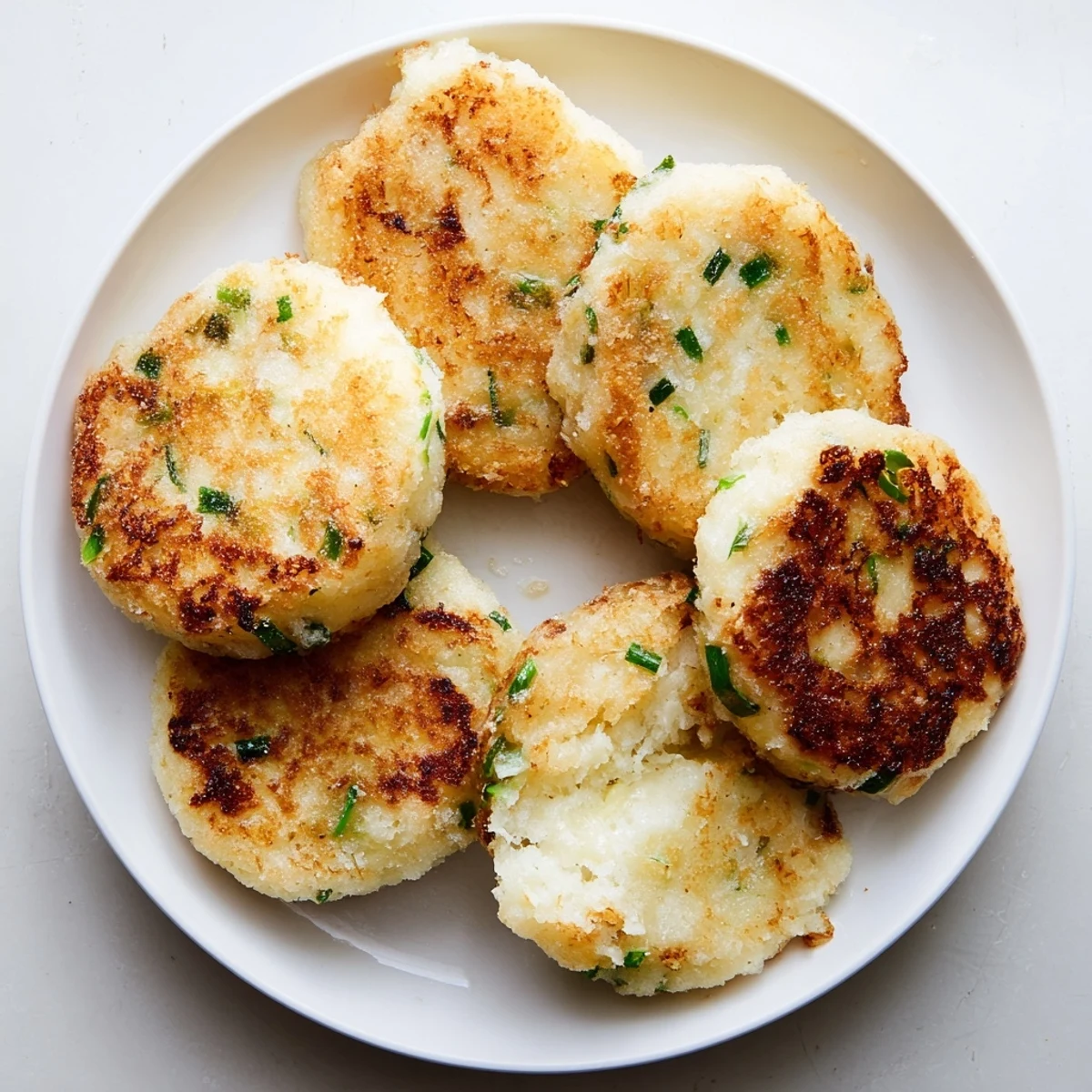 Golden, pan-fried Irish Potato Cakes with Scallions fresh from the skillet, showing crisp edges and a soft, steamy interior.  