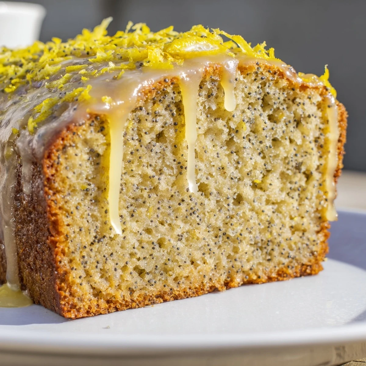 Freshly baked Lemon Poppy Seed Loaf on a wooden board, dusted with powdered sugar and served with a cup of tea.