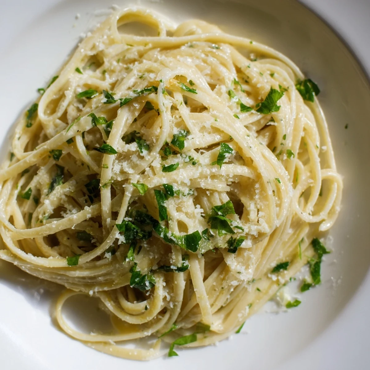 A close-up of Creamy Garlic Pasta with Fresh Herbs twirled on a fork over a white plate.