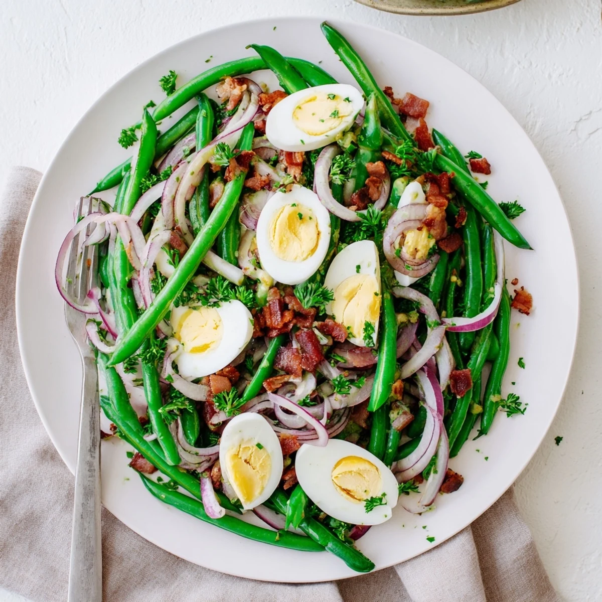 Freshly prepared Green Bean, Bacon, and Egg Salad in a white bowl, garnished with chopped parsley and a tangy vinaigrette.