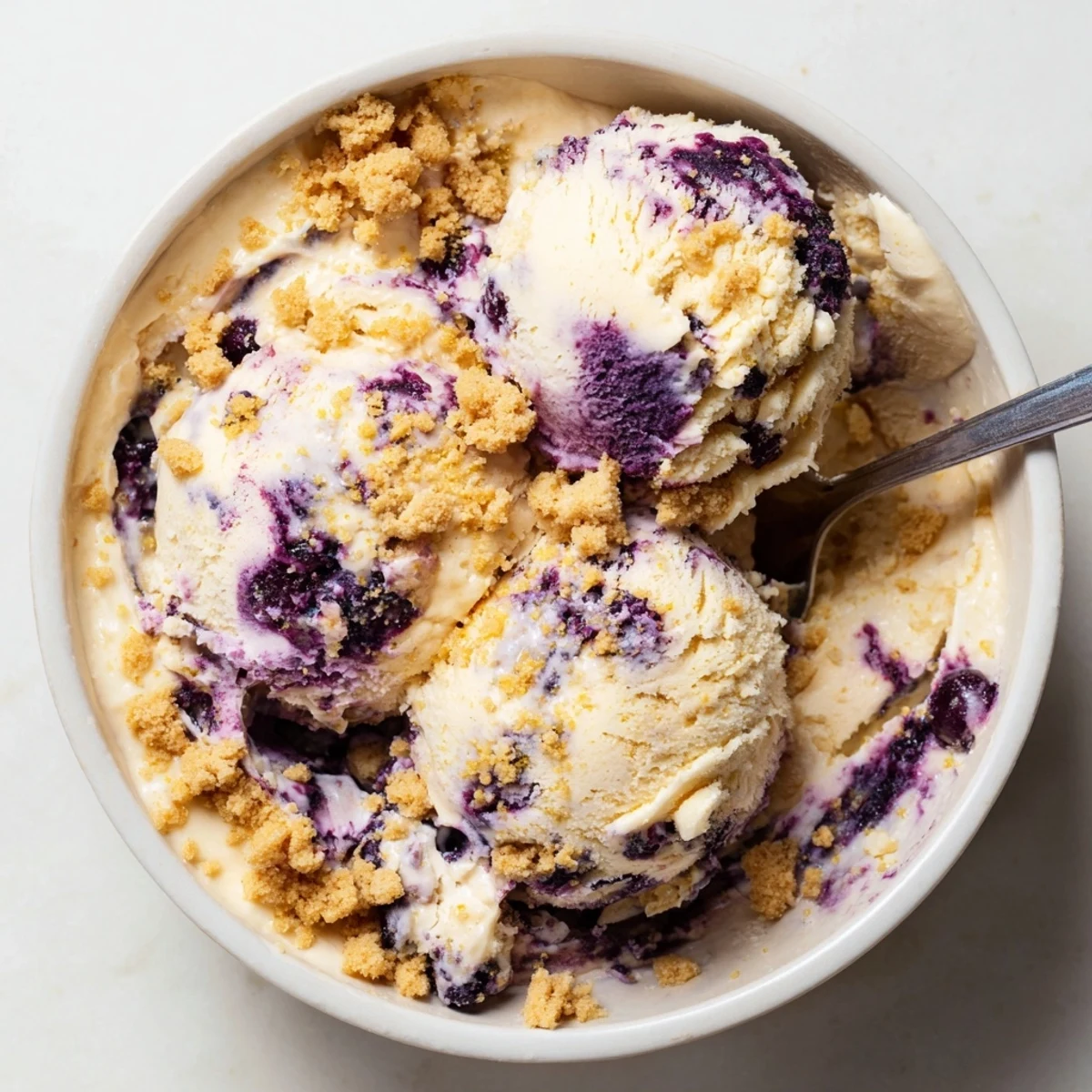 Close-up photo of homemade Lemon Blueberry Cheesecake Ice Cream, highlighting bright blueberries, lemon zest flecks, and rich cheesecake swirls in a freezer-safe container.