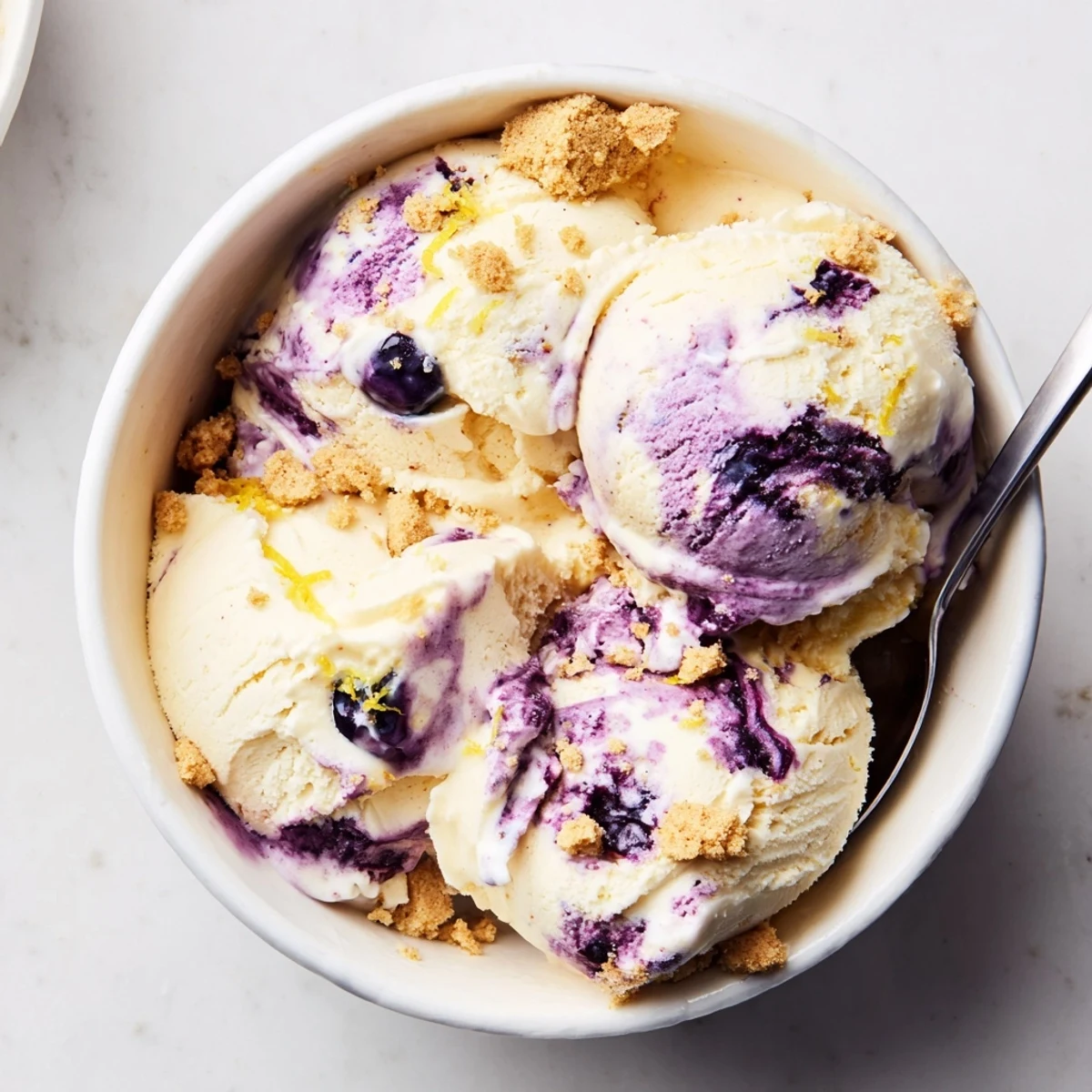 Creamy Lemon Blueberry Cheesecake Ice Cream in a dessert dish, topped with fresh berries and a drizzle of blueberry sauce, perfect for summer gatherings.