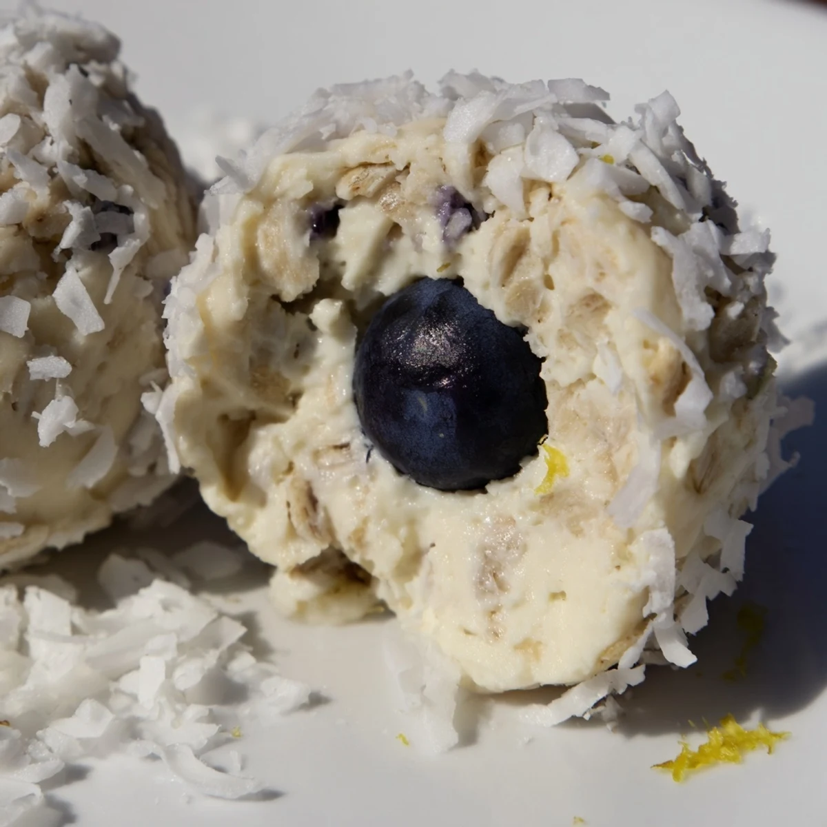 A close-up of Lemon Blueberry Cottage Cheese Protein Bites, coated in coconut, highlighting their bright zest and juicy berry filling, perfect for a post-workout treat.
