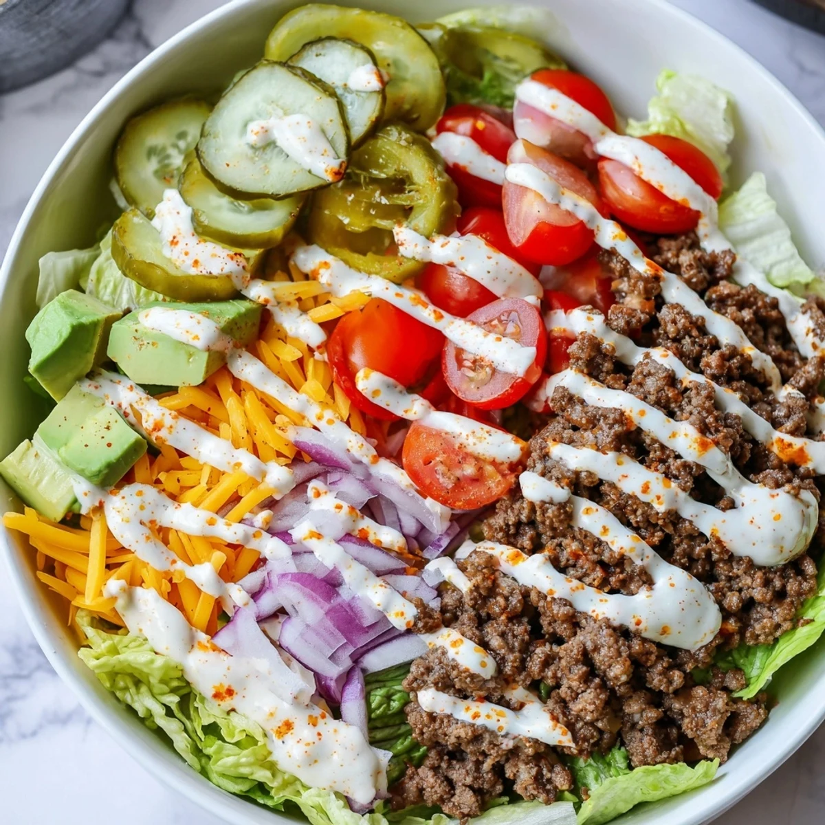 Protein-packed burger bowl served in a white dish with fluffy lettuce, savory spiced beef, colorful tomato halves, shredded sharp cheddar, and dill pickle garnish.