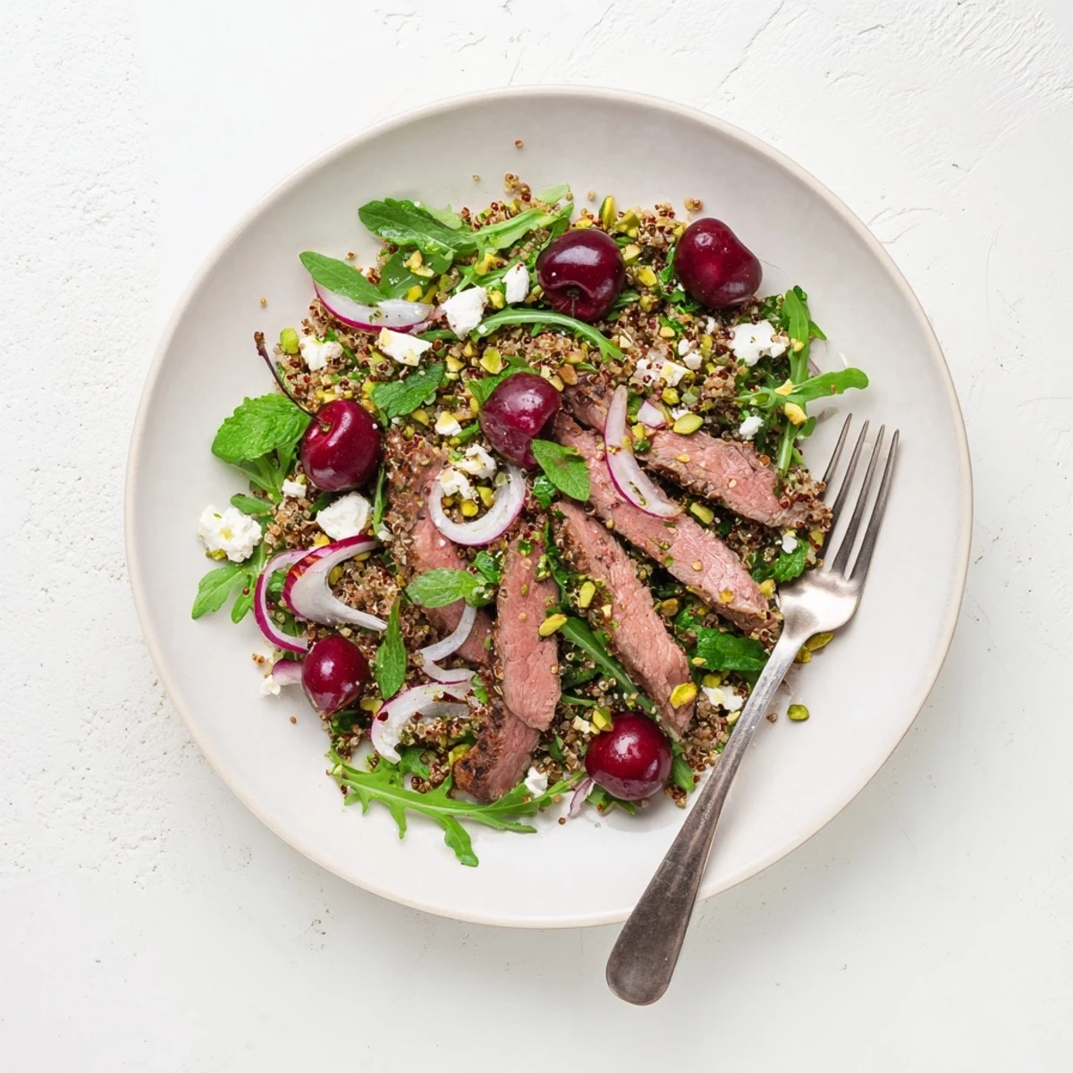 Mediterranean-inspired salad featuring spiced lamb, sweet cherries, and toasted pistachios on quinoa