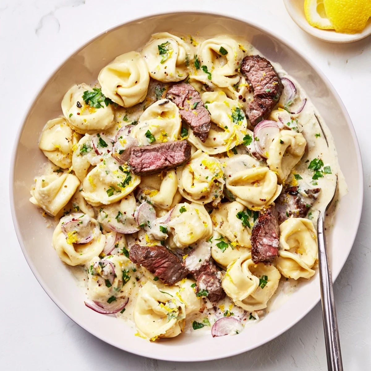 Garlic steak tortellini in a creamy white sauce with fresh parsley garnish on a white plate