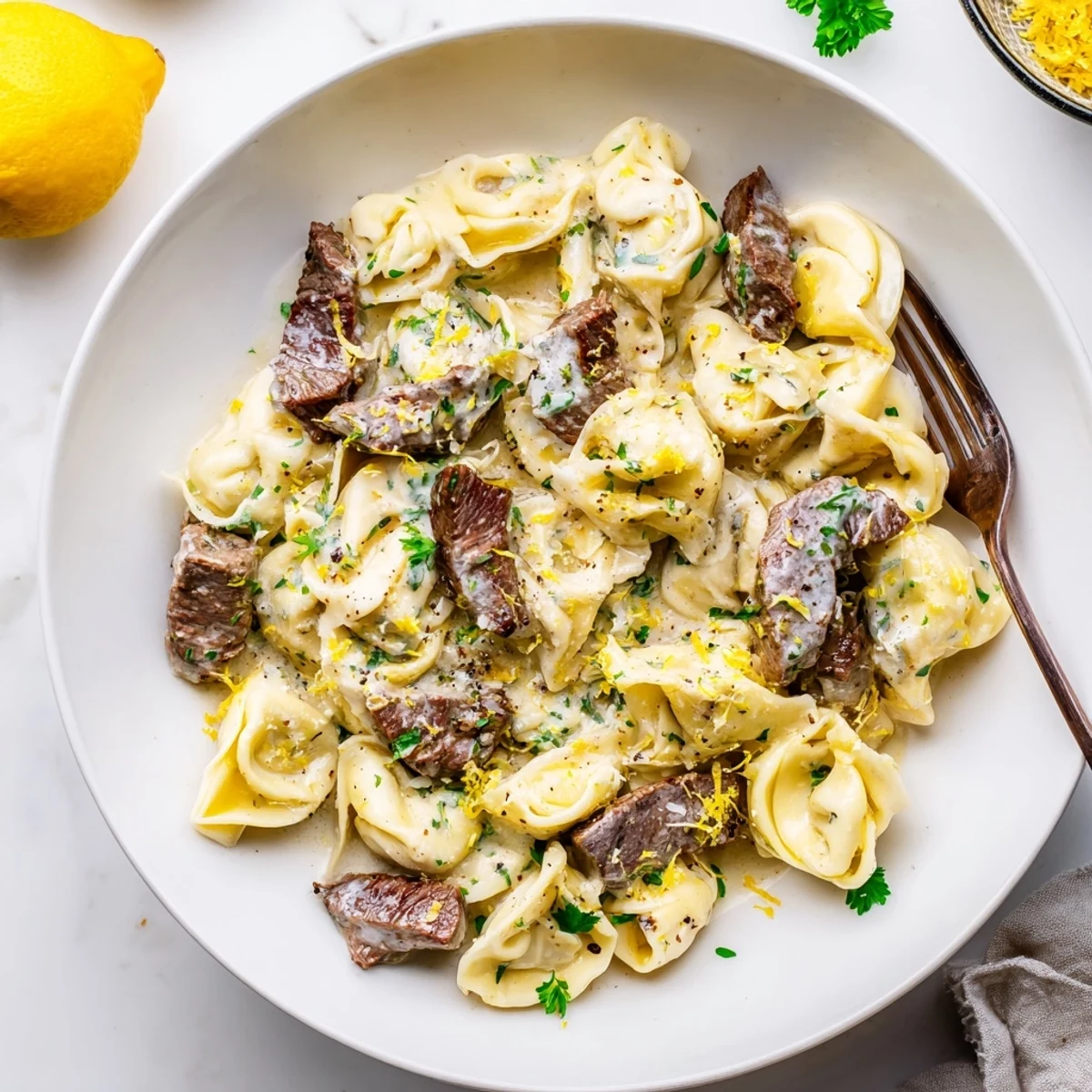 Sliced seared steak mixed with cheese tortellini in a rich garlic cream sauce with lemon zest