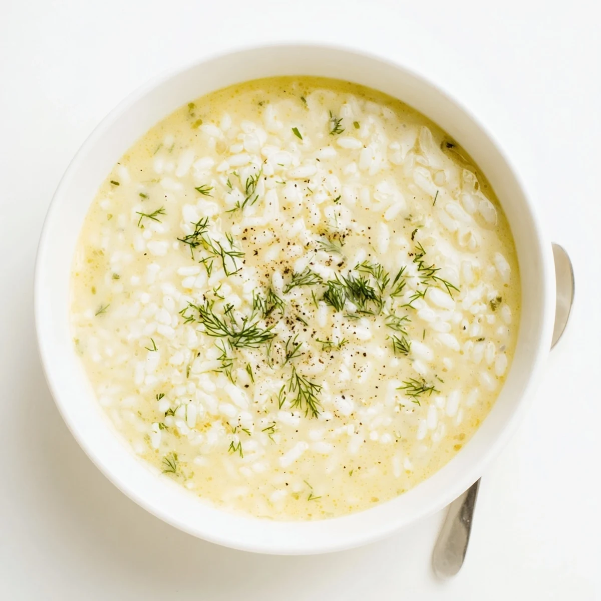 Steaming bowl of classic Greek egg and lemon soup garnished with fresh dill and cracked black pepper