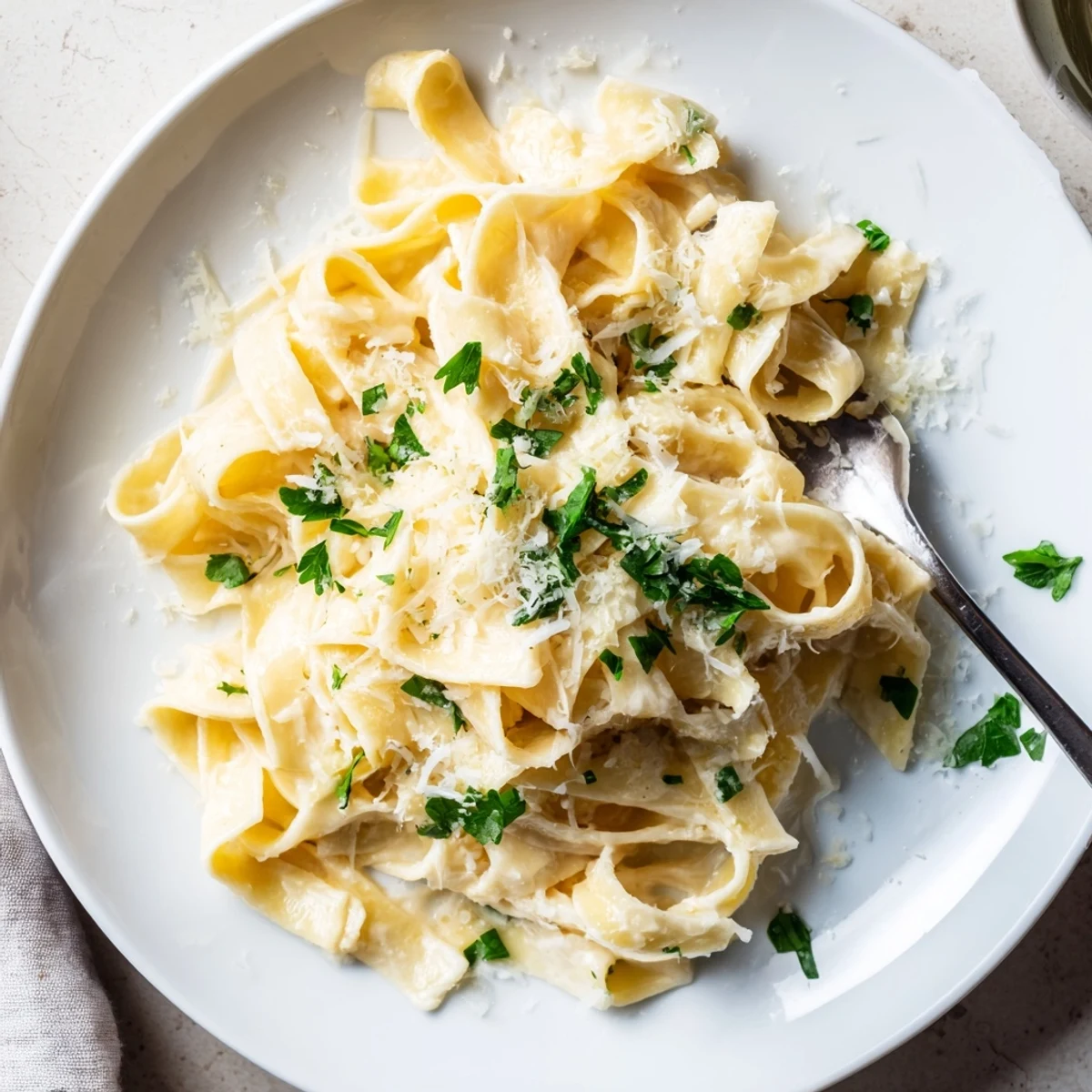 Creamy fettuccine Alfredo plated with parsley garnish and extra shredded Parmesan on top