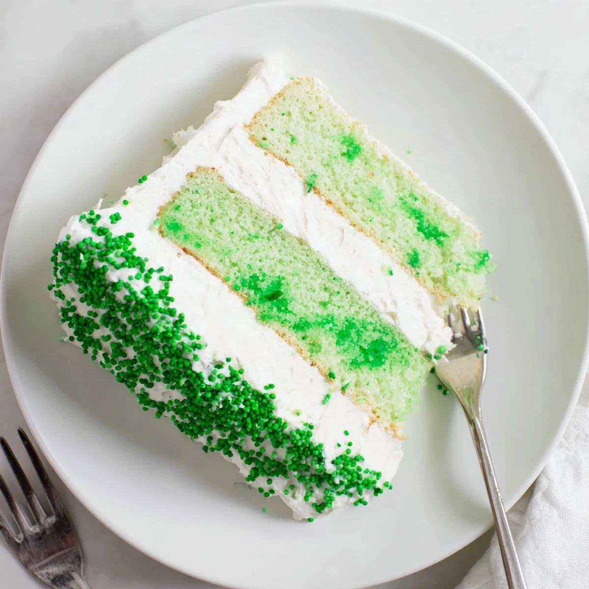 Slices of green St. Patricks Day cake revealing moist colored layers and whipped vanilla frosting