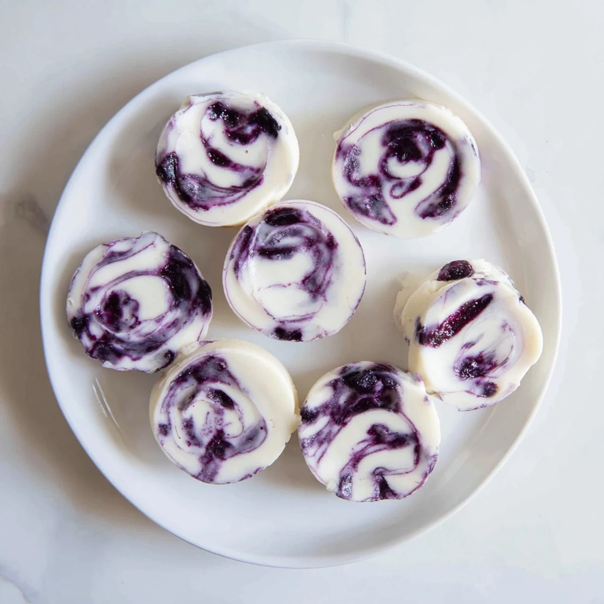 Frozen blueberry swirl yogurt bites arranged on a white plate with vibrant purple berry ribbons throughout the creamy Greek yogurt
