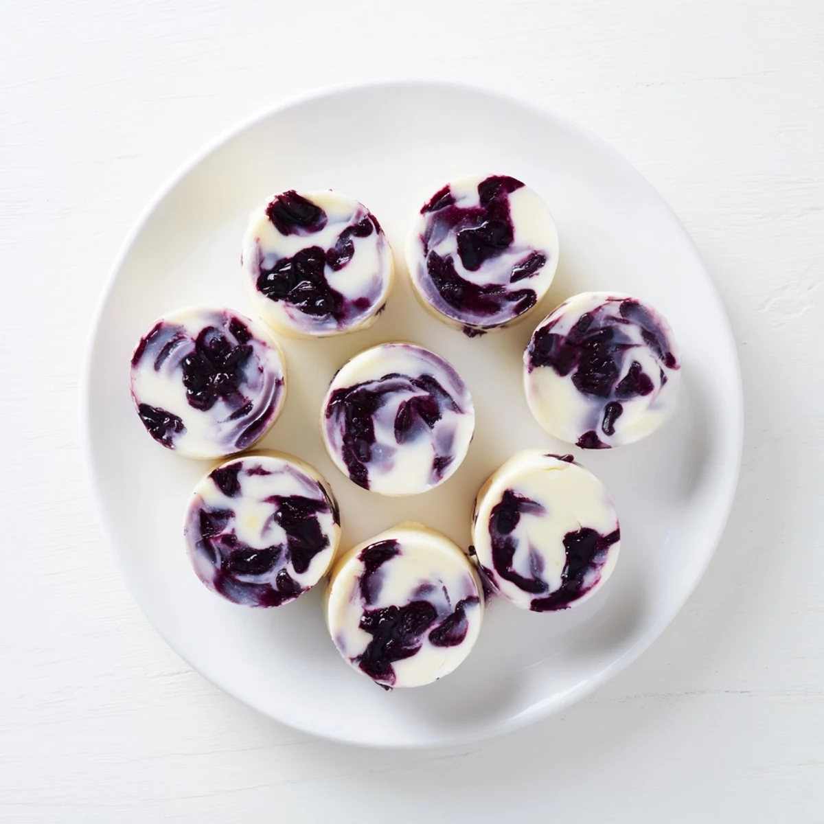 Refreshing blueberry swirl yogurt bites stacked neatly on a baking sheet, featuring thick purple berry swirls against white creamy yogurt
