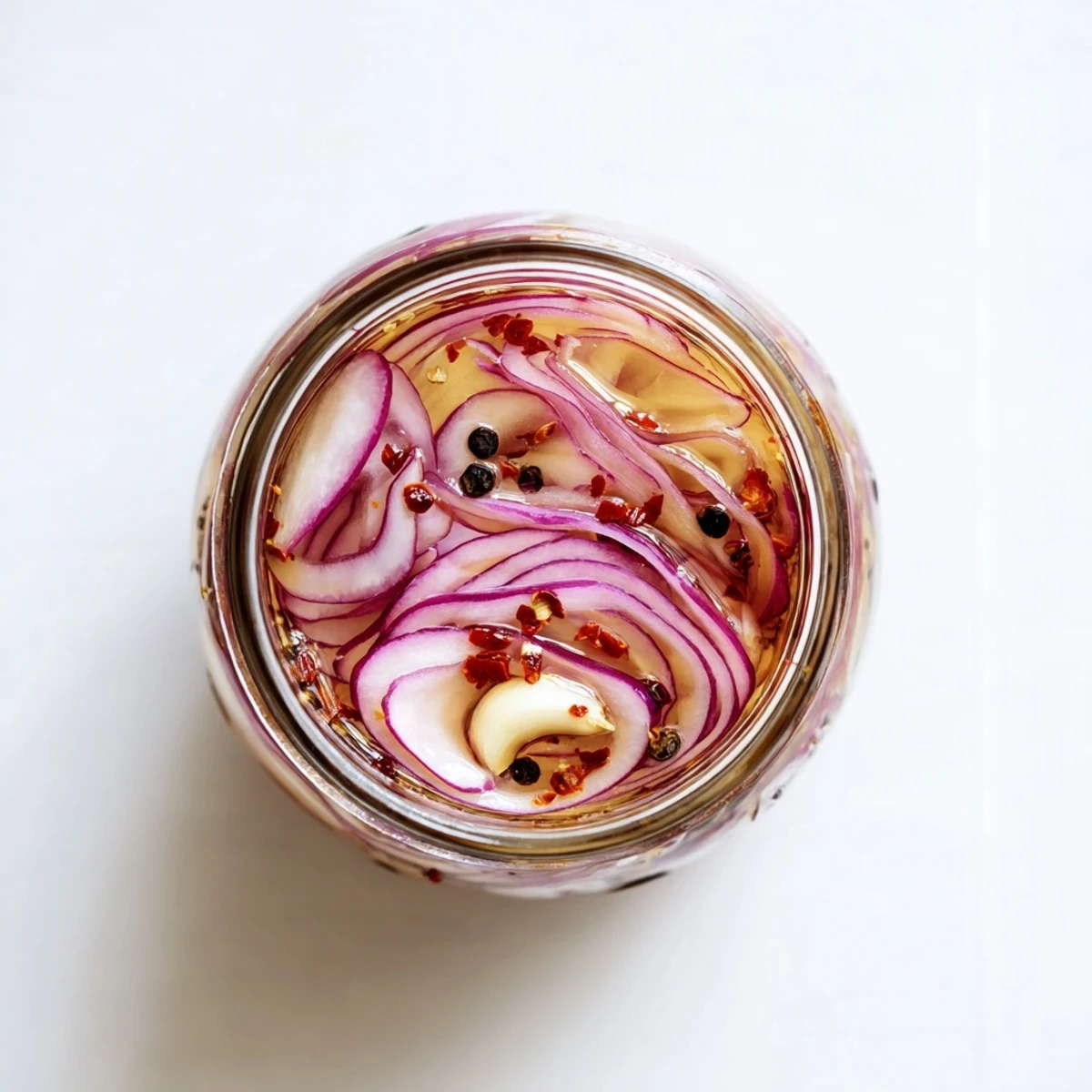 Glass jar filled with vibrant hot honey pickled red onions suspended in golden brine