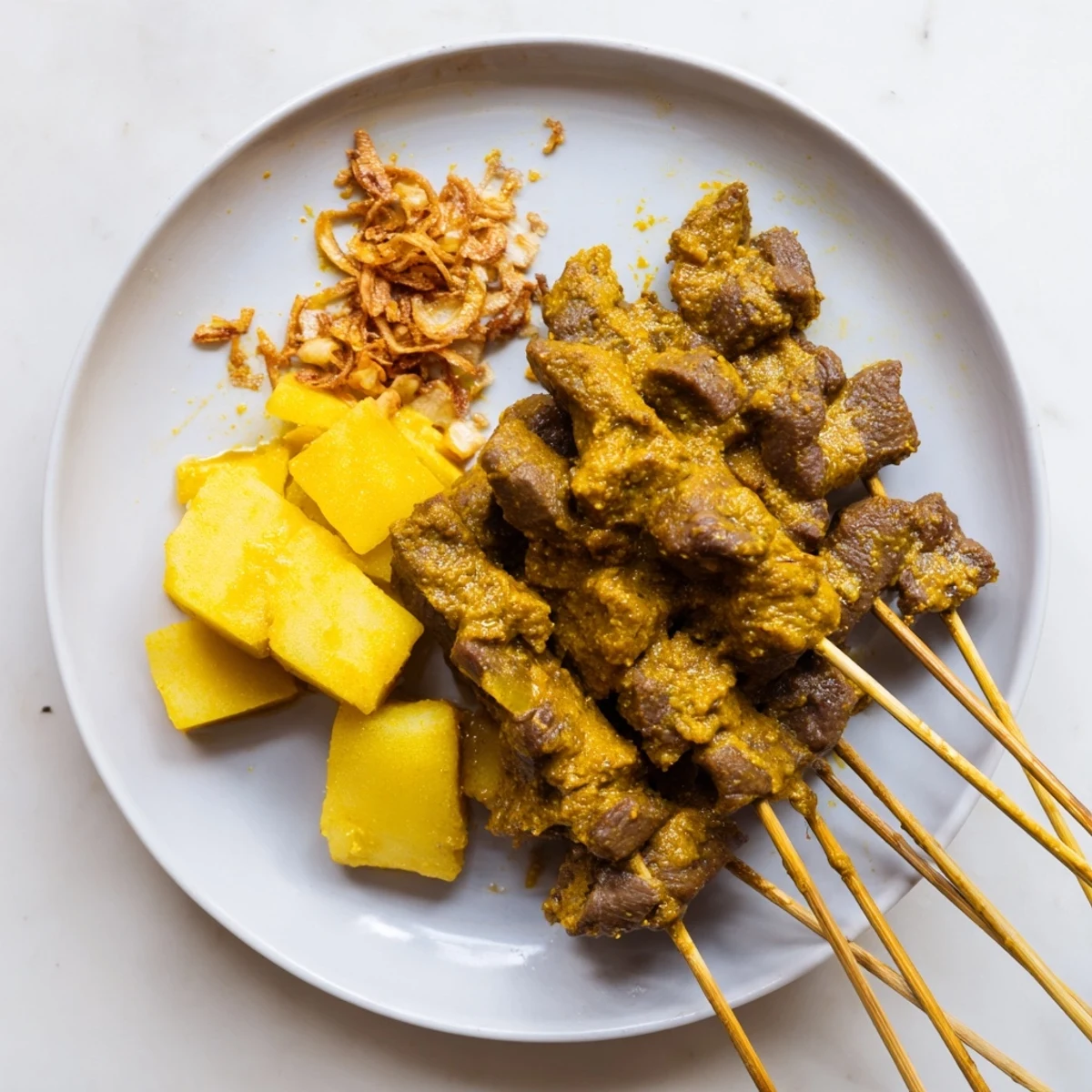 Charcoal-grilled Sate Padang beef skewers plated with rich aromatic turmeric sauce and sliced rice cake