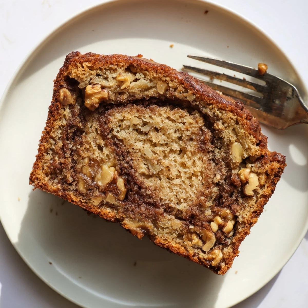 Thick slice of warm banana bread with cinnamon swirl topped with chopped walnuts