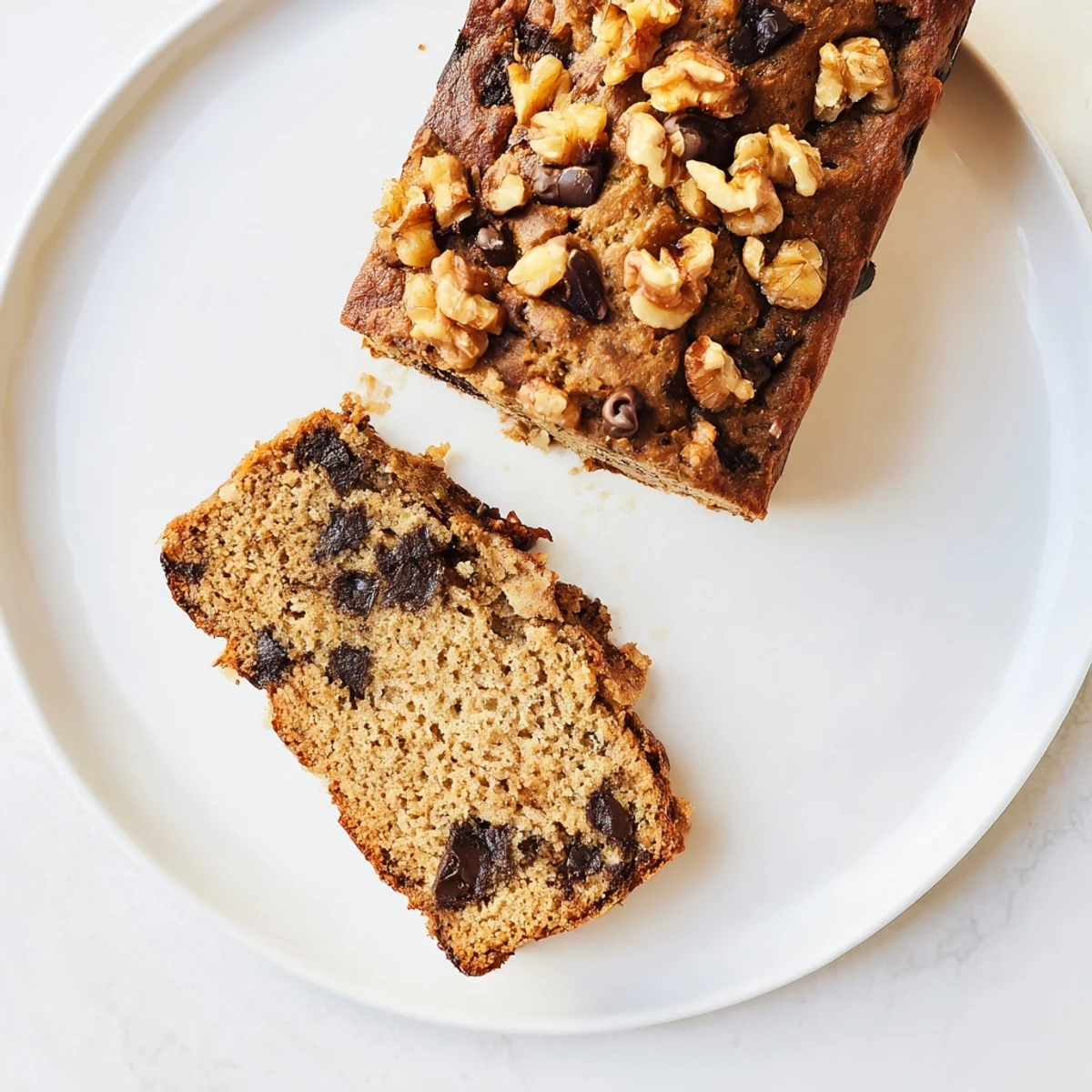 Thick slice of moist protein banana bread oil free topped with dark chocolate chips on a white plate