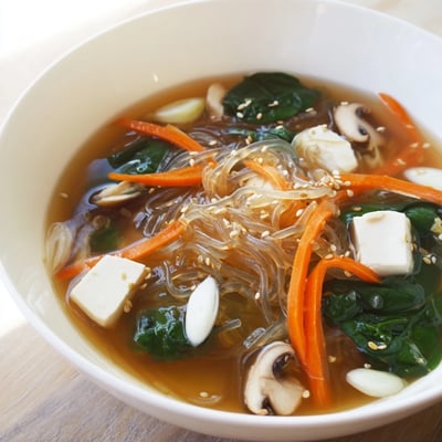 Steaming Japanese Harusame Noodle Soup served in a rustic ceramic bowl with julienned carrots and leafy greens.
