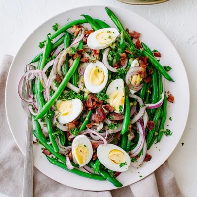 Freshly prepared Green Bean, Bacon, and Egg Salad in a white bowl, garnished with chopped parsley and a tangy vinaigrette.